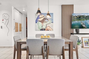 A modern dining area with a glass table, grey upholstered chairs, and a painting of a woman with a hat. - Modern Chic Retreat | Near Ferry & Beach | Pool (Ceiba)