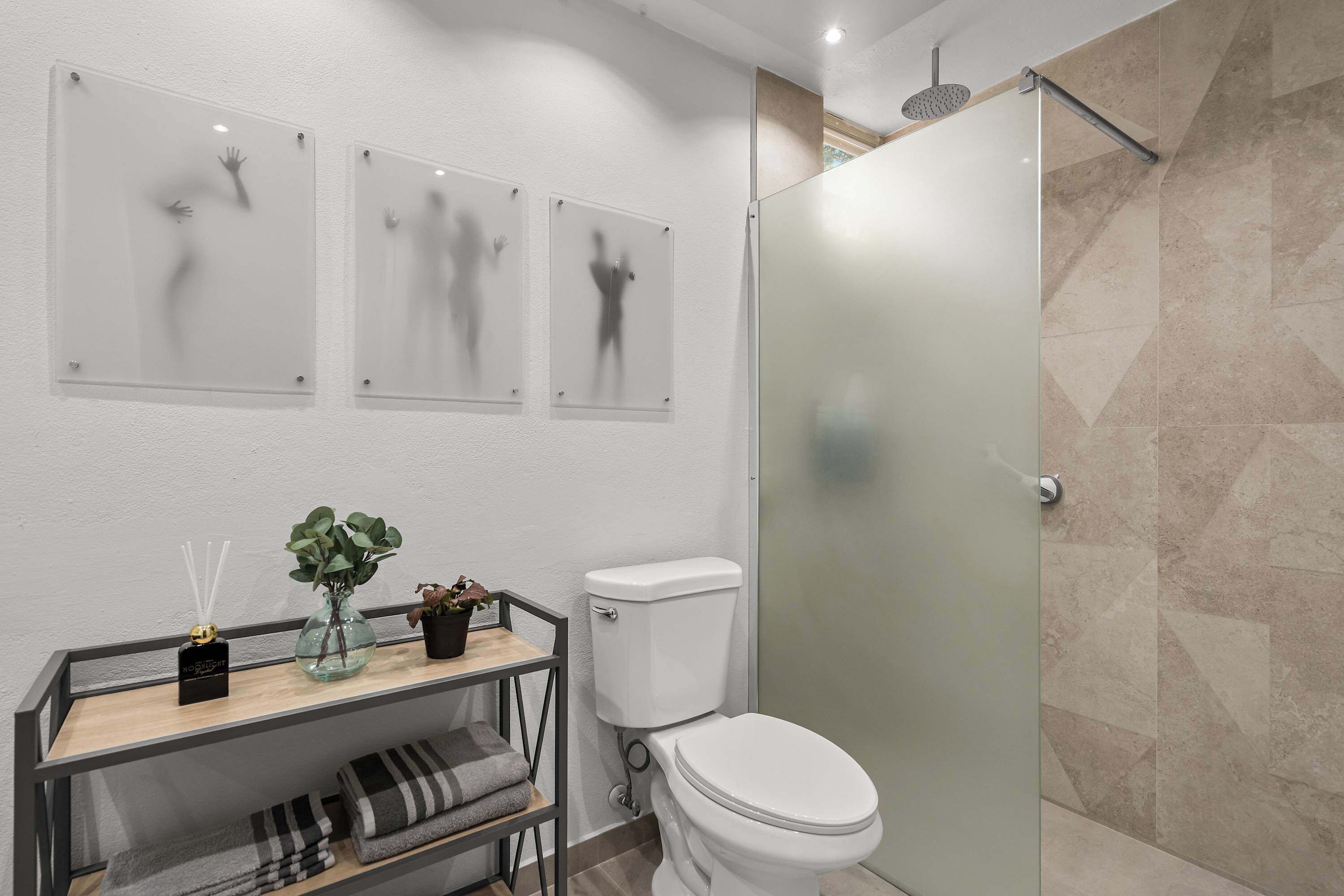 Une salle de bain moderne équipée de toilettes, d’une douche à parois de verre et d’un meuble-lavabo agrémenté d’une plante et d’un vaporisateur d’air.