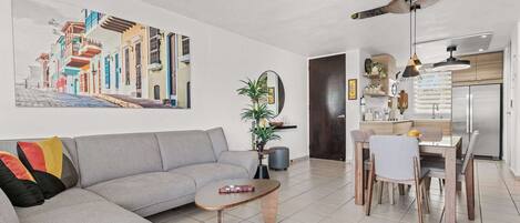 A modern living room with a gray sofa, a wooden coffee table, and a dining area with a wooden table and chairs.