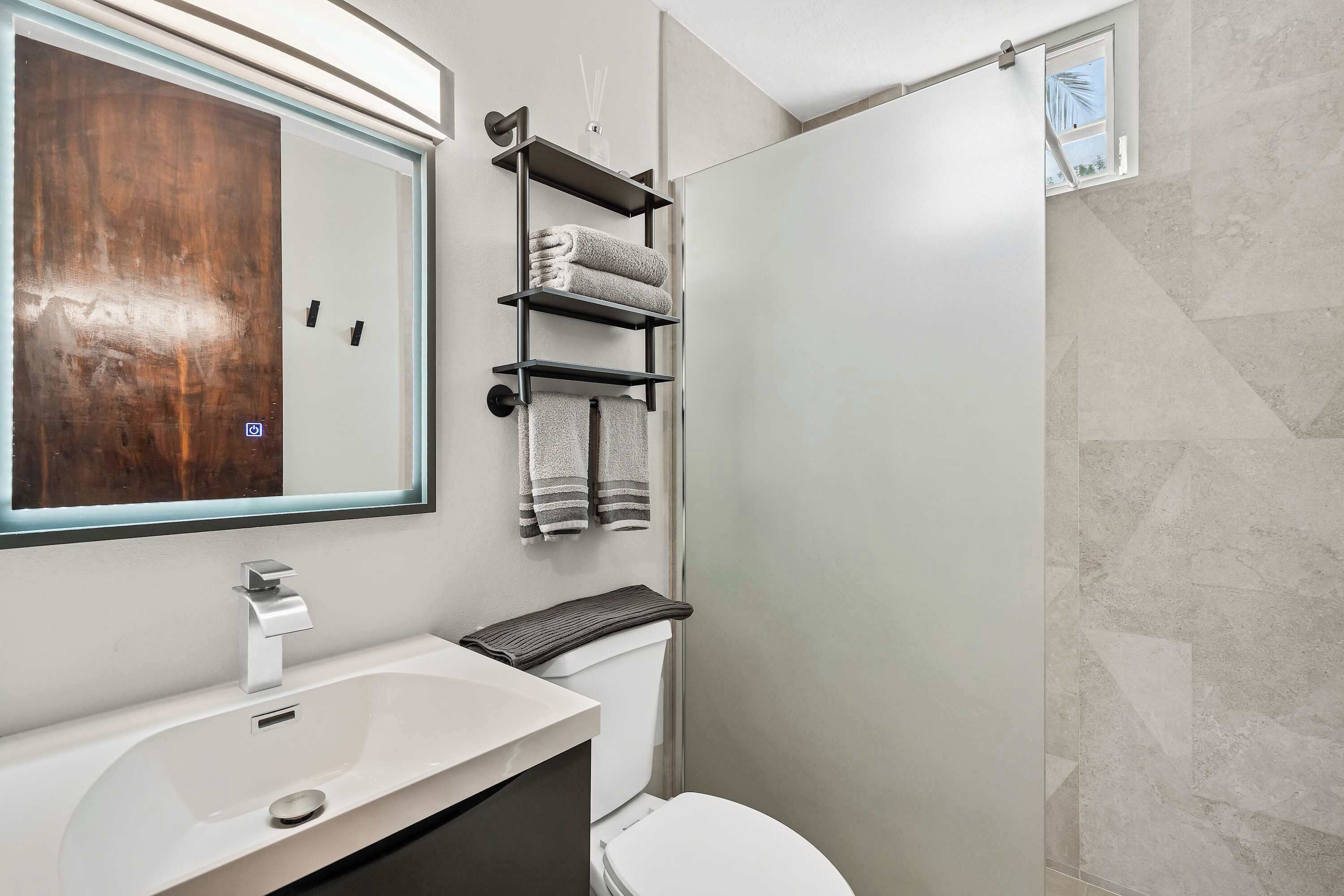 A modern bathroom with a large mirror, a white sink, a toilet, and a shower area.