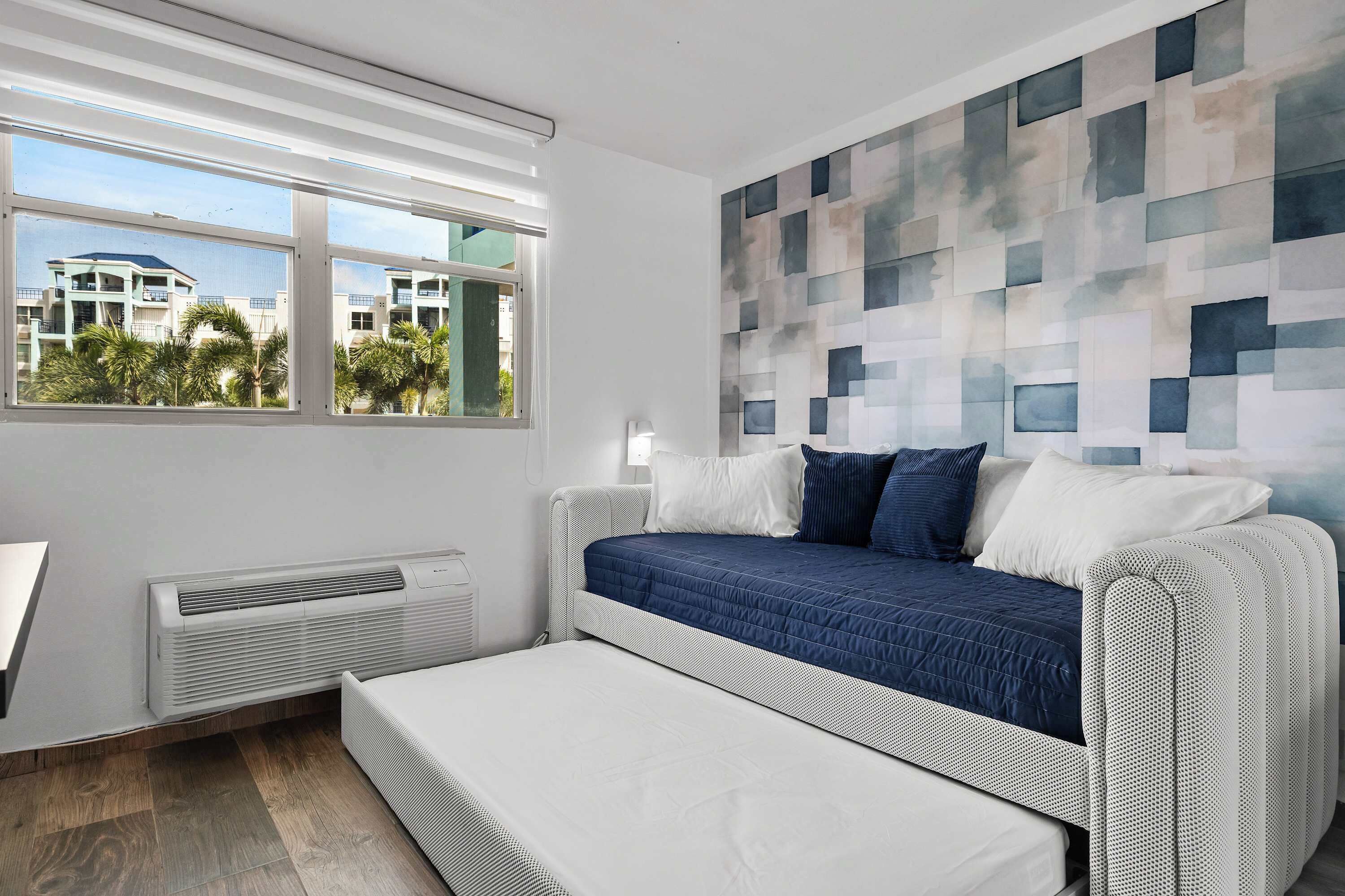 Un dormitorio moderno con cama, un banco, una ventana y una pared con diseño geométrico.
