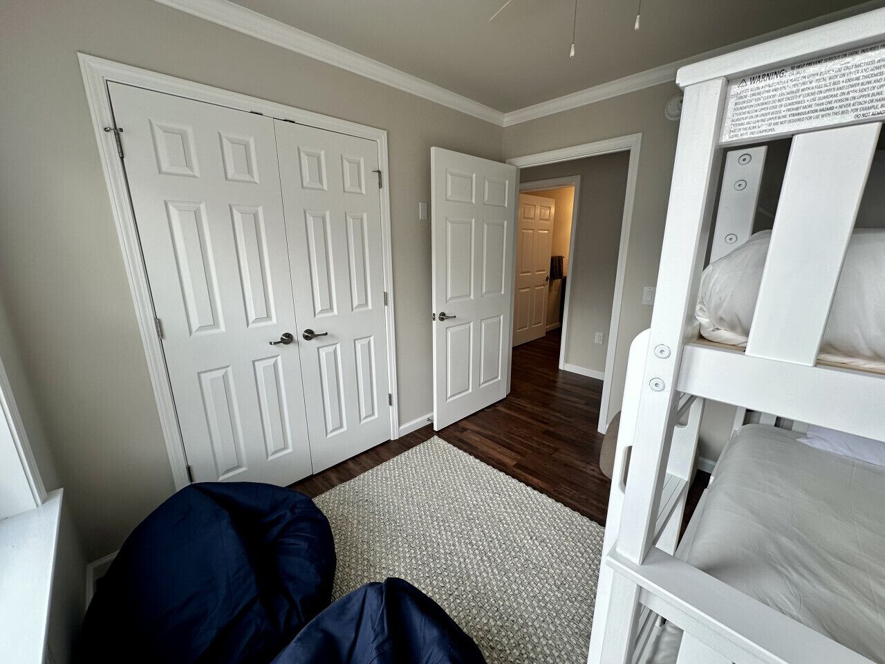 A room with a bunk bed, two white doors, a hallway, and a wooden floor.