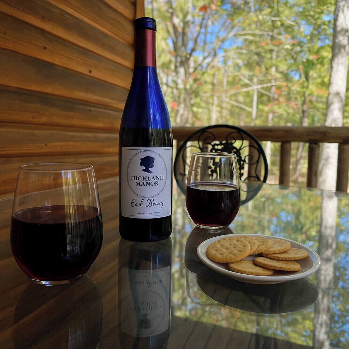 A bottle of Highland Manor Cock Berry wine, two glasses, and a plate of crackers on a table.
