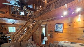 L’intérieur d’une cabane comprend un escalier en bois, des canapés en cuir, un coin repas et une cheminée.
