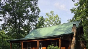 Une cabane en rondins avec un porche, une cheminée et une petite terrasse.