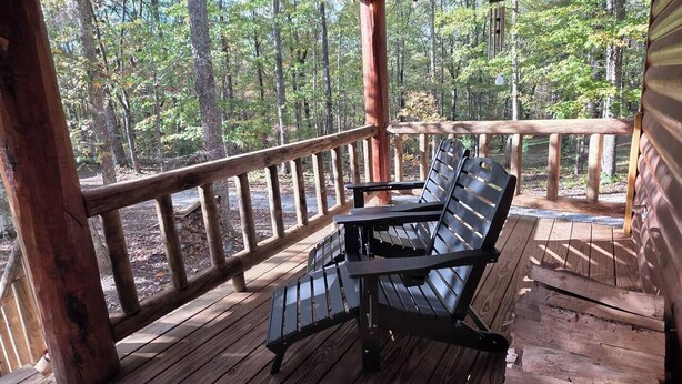 Une terrasse en bois avec deux chaises noires, entourée d’une balustrade en bois, donnant sur une forêt.