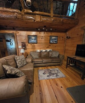 Ein gemütliches Blockhaus-Interieur mit einer Sofagarnitur, einem Fernseher und einem Kamin.