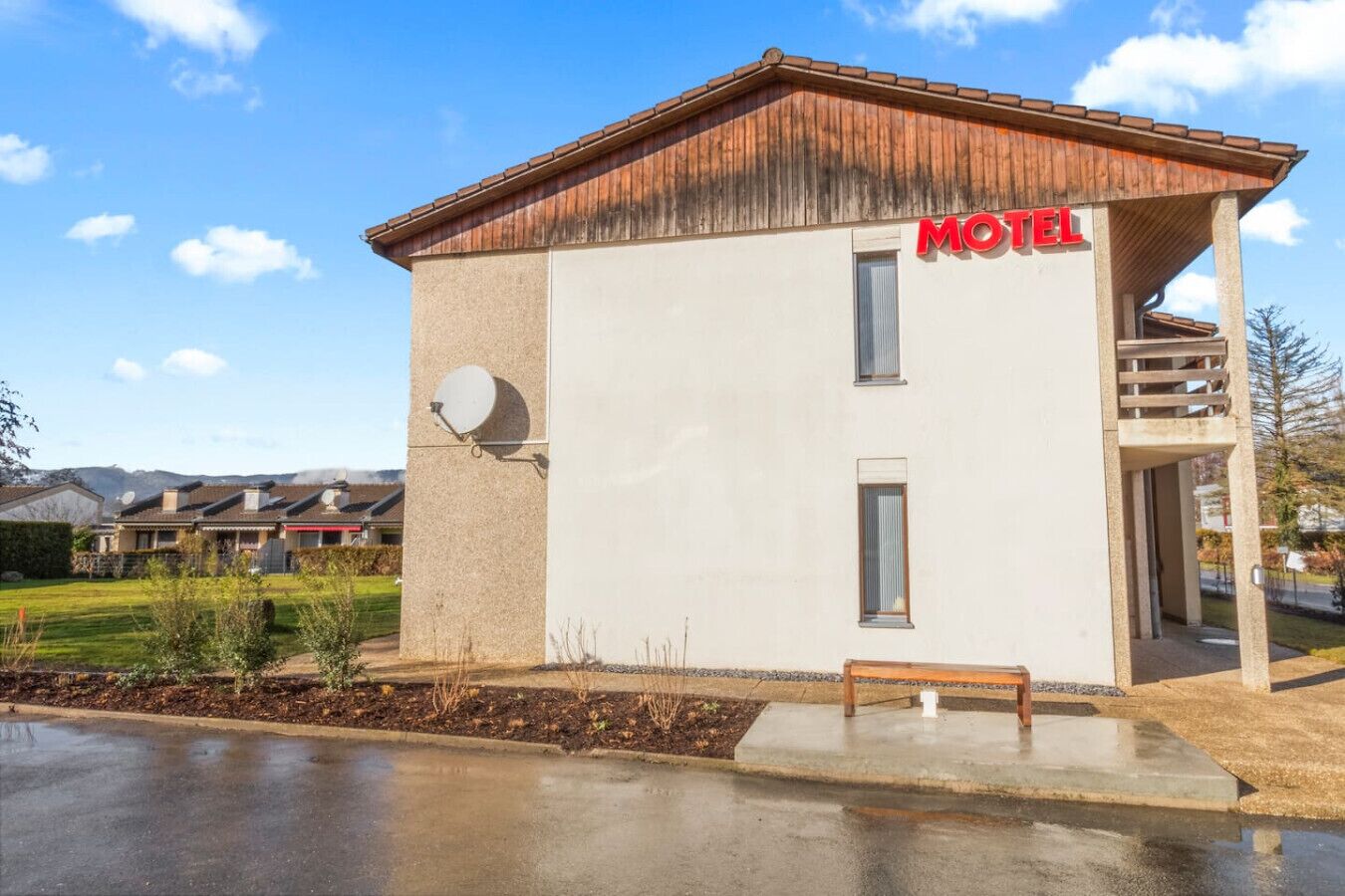 A small, single-story motel with a red "MOTEL" sign, a satellite dish, and a small outdoor seating area.