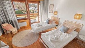Une chambre avec deux lits simples, un tapis rond, une chaise avec une couverture et une vue sur l’extérieur.