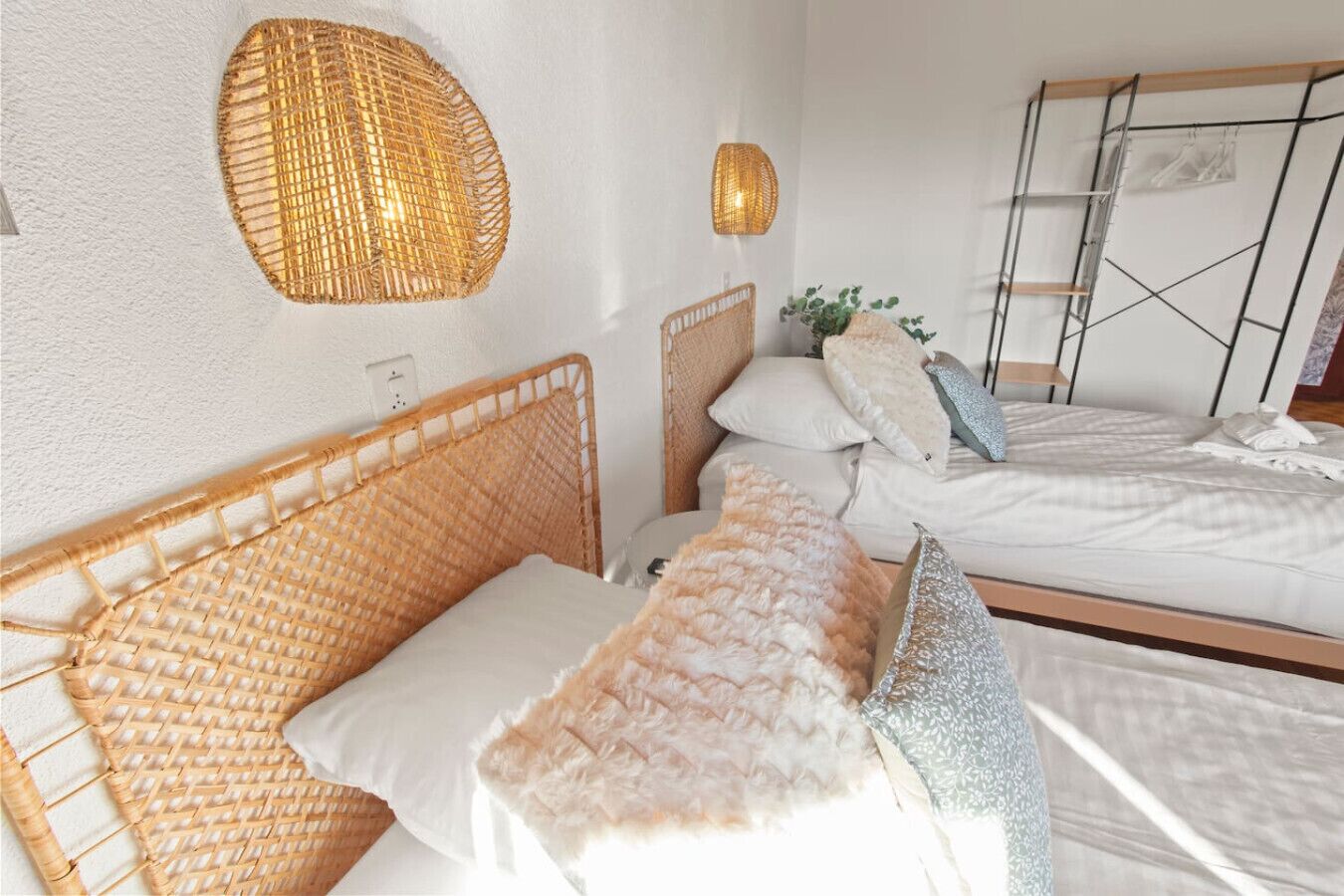 Ein Zimmer mit zwei Betten, Korbhaupten, weißer Bettwäsche und einer gewobenen Wandleuchte.