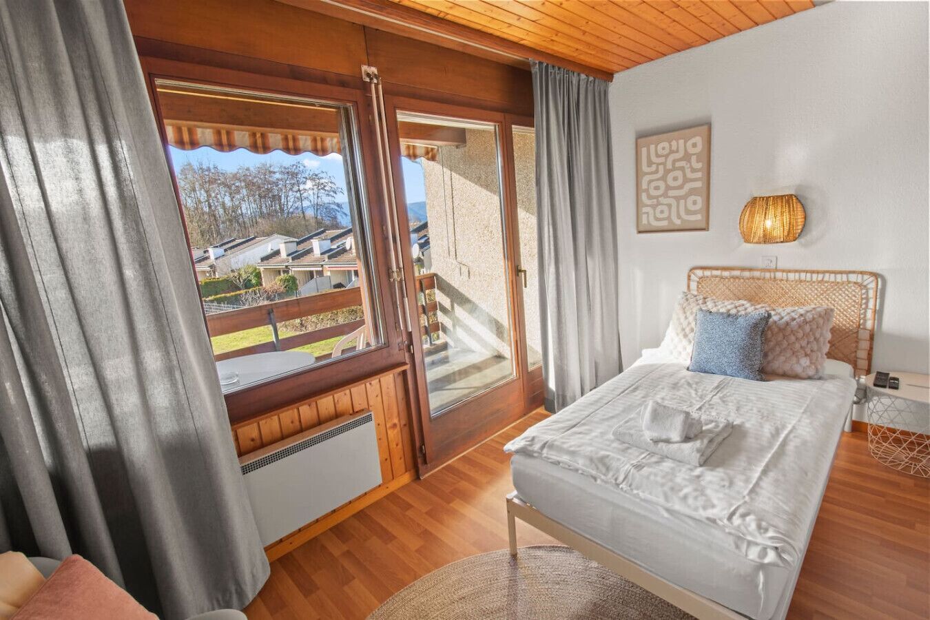 A bedroom with a large bed, a view of a balcony, and a wooden ceiling.