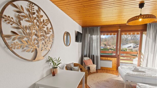 Une pièce chaleureuse avec un plafond en bois, une table ronde, un lit et une grande fenêtre avec des rideaux.
