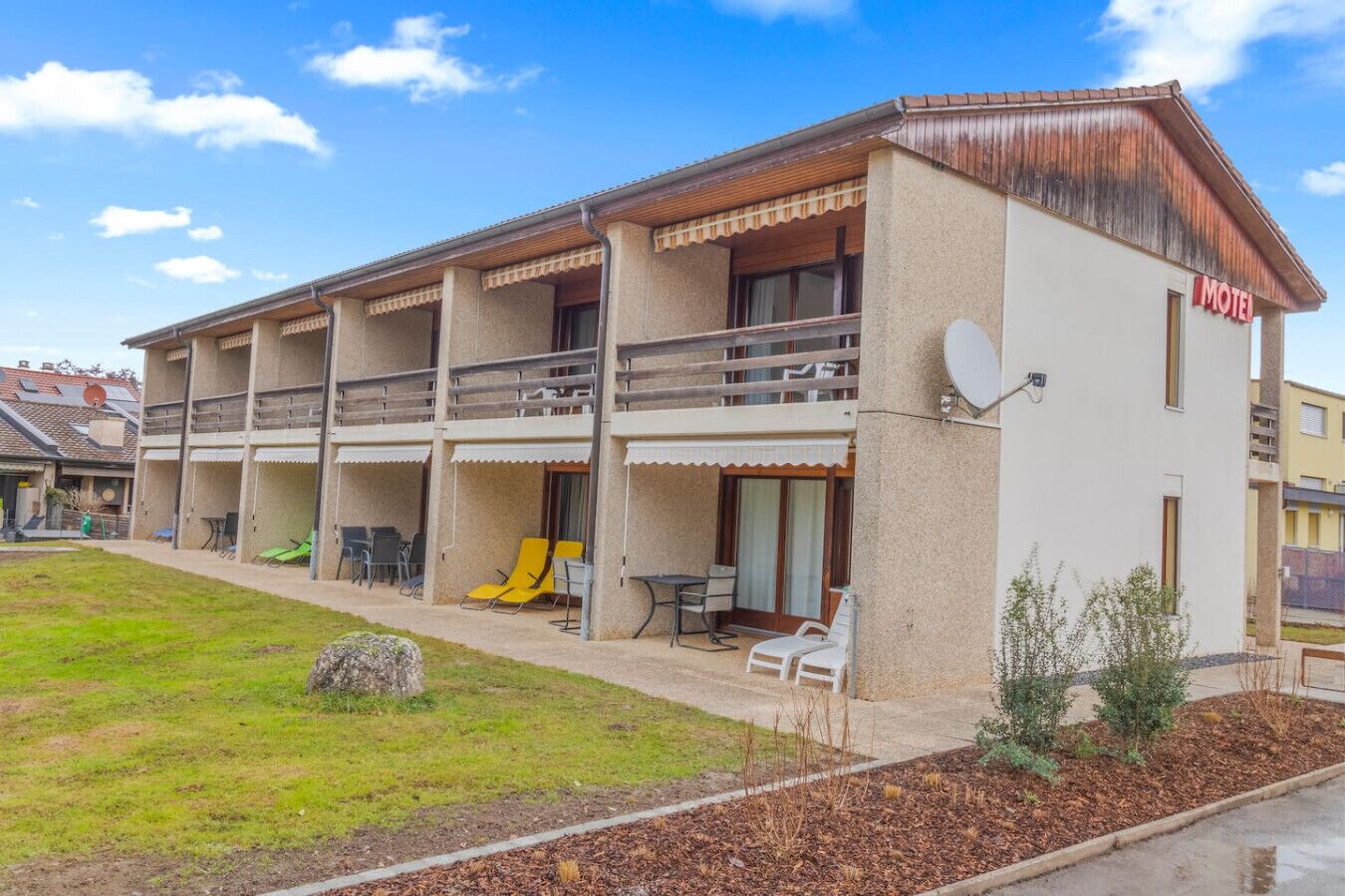 A two-story motel with a balcony on the upper floor, outdoor seating, and a small garden area.
