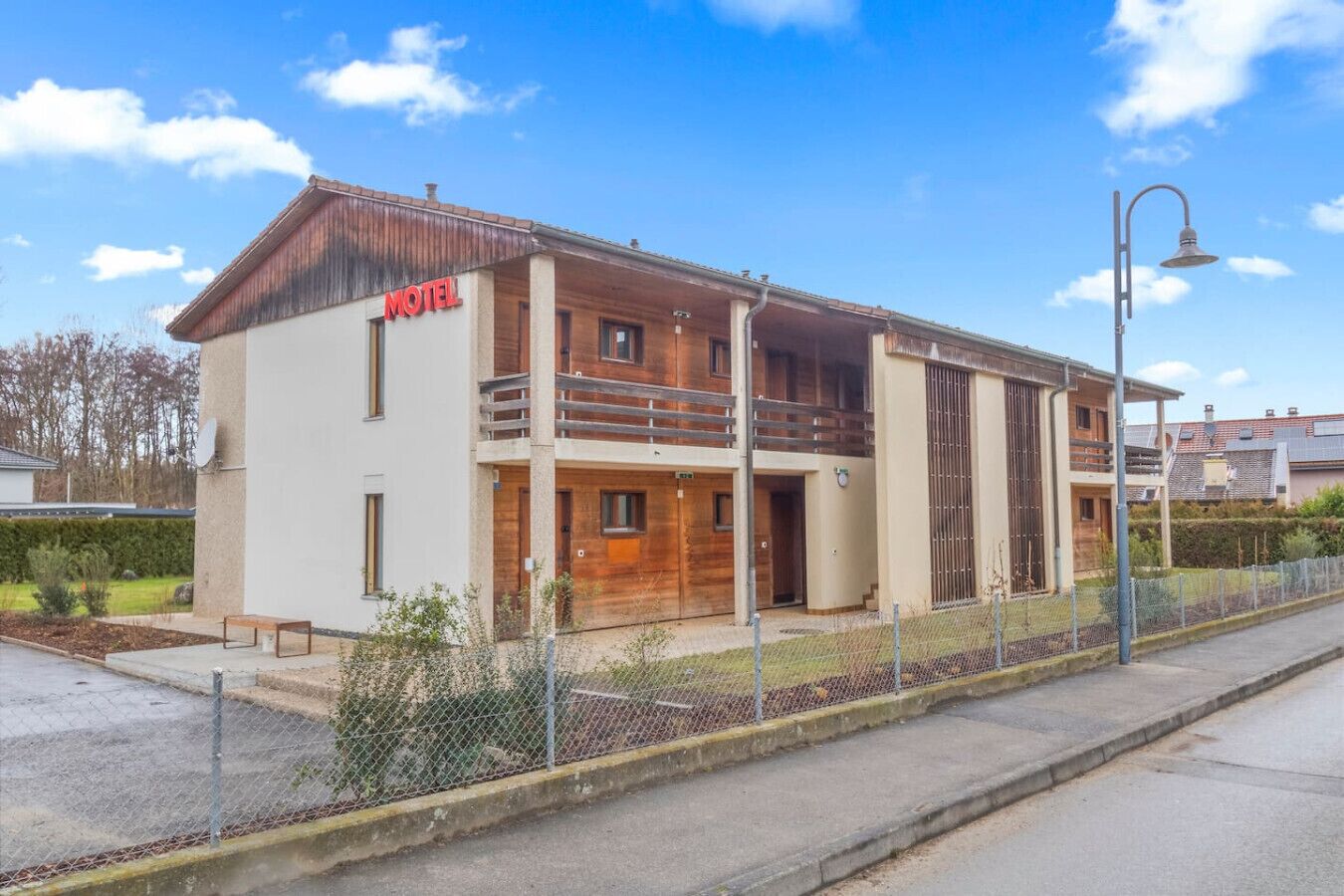 A two-story motel with a wooden facade, a balcony on the upper floor, and a fenced parking area.