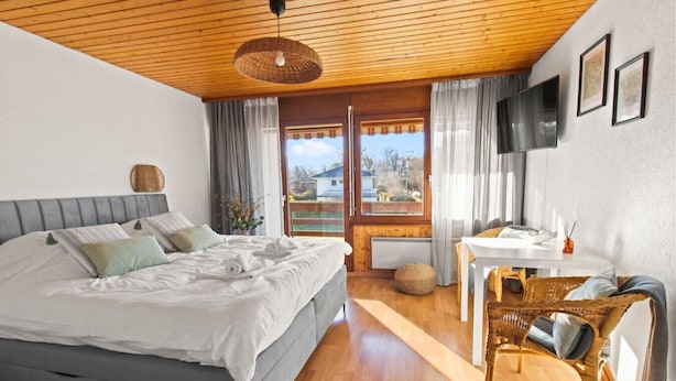 A bedroom with a bed, a desk, a chair, and a window with curtains.
