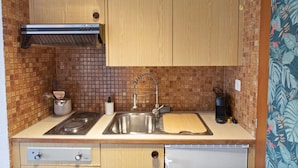 A compact kitchen with wooden cabinets, a stainless steel sink, a gas stove, and a microwave.