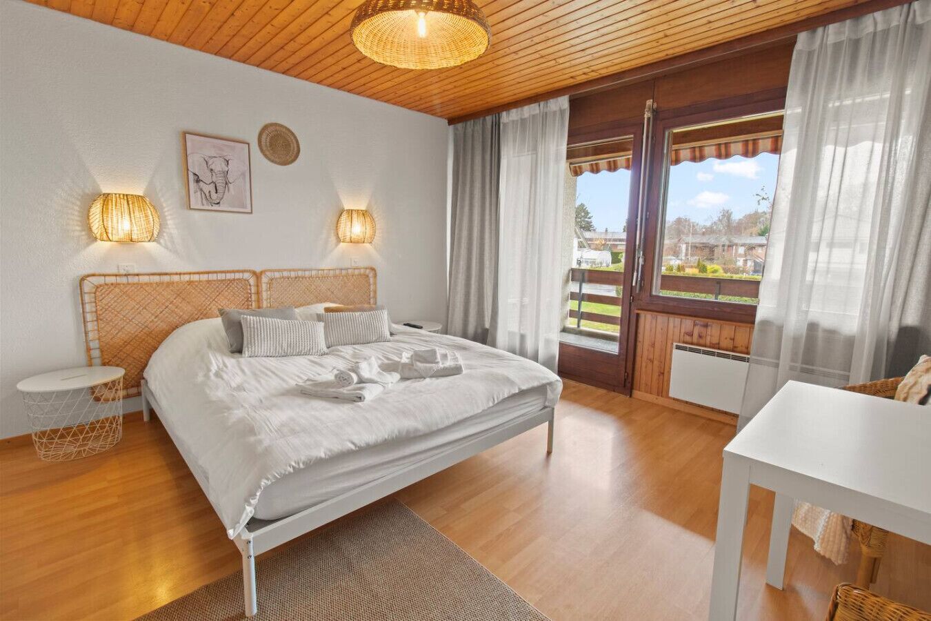 Un dormitorio con una cama grande, dos lámparas de noche, techo de madera y vistas al exterior a través de una ventana.