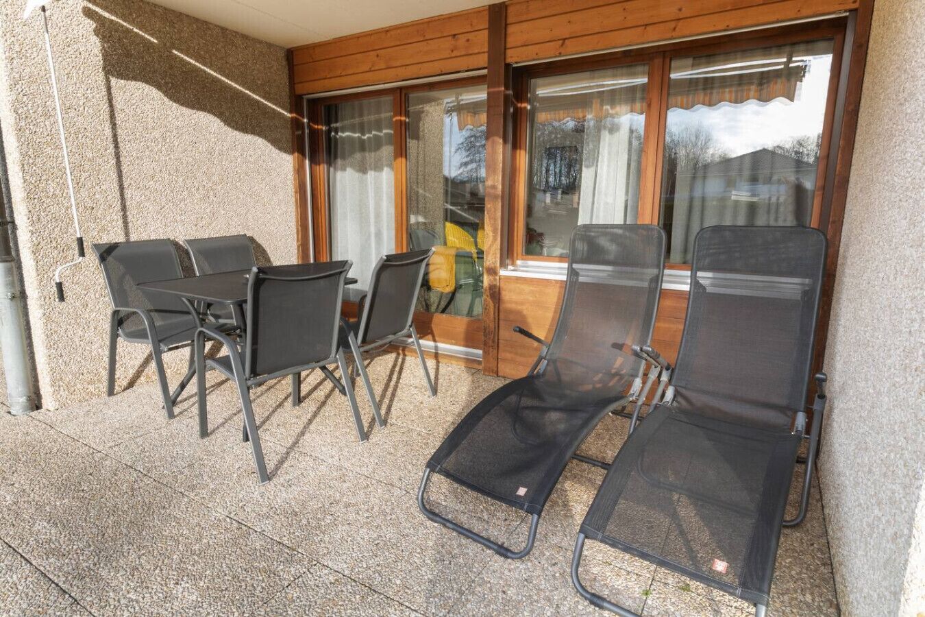 A patio with a table and chairs, a sun lounger, and a glass door leading to a room.