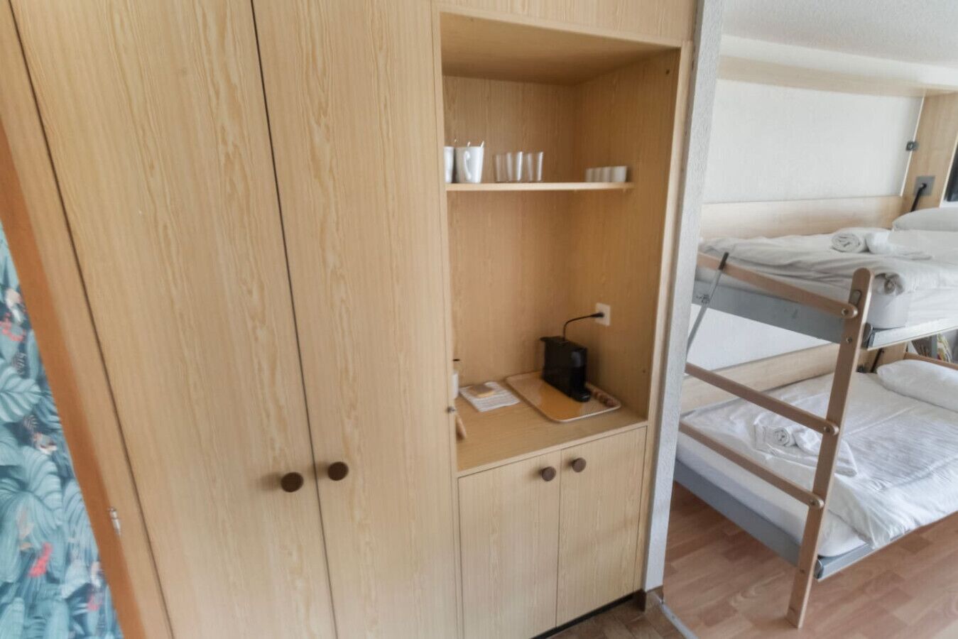 Ein Etagenbett mit einem Holzschrank daneben, der ein Fach mit Tassen und eine Steckdose enthält.