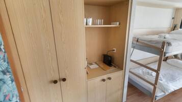 Ein Etagenbett mit einem Holzschrank daneben, der ein Fach mit Tassen und eine Steckdose enthält.