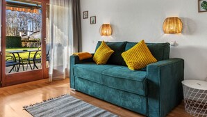 Un canapé de couleur bleu sarcelle agrémenté de coussins jaunes, un tapis gris et une lampe en osier sur un mur blanc.