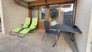 Ett takförsett utomhusområde med sittplatser, bestående av två gröna loungestolar och ett bord.