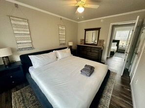 A neatly made bed with white linens, a dark headboard, and a folded towel on the foot of the bed. There is a nightstand with a lamp and a wall hanging above the bed. - Summit Vista Lodge - Breathtaking 180°+ Mountain Views | Hot Tub (Waynesville)
