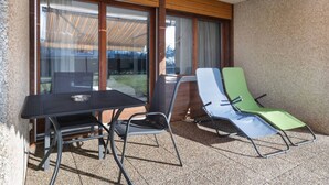 Un balcon avec une table et des chaises, de grandes fenêtres et une vue sur une maison.