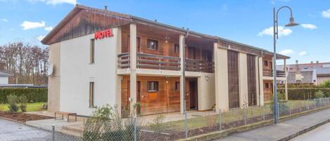 A two-story motel with a wooden facade, a balcony on the upper floor, and a fenced parking area.