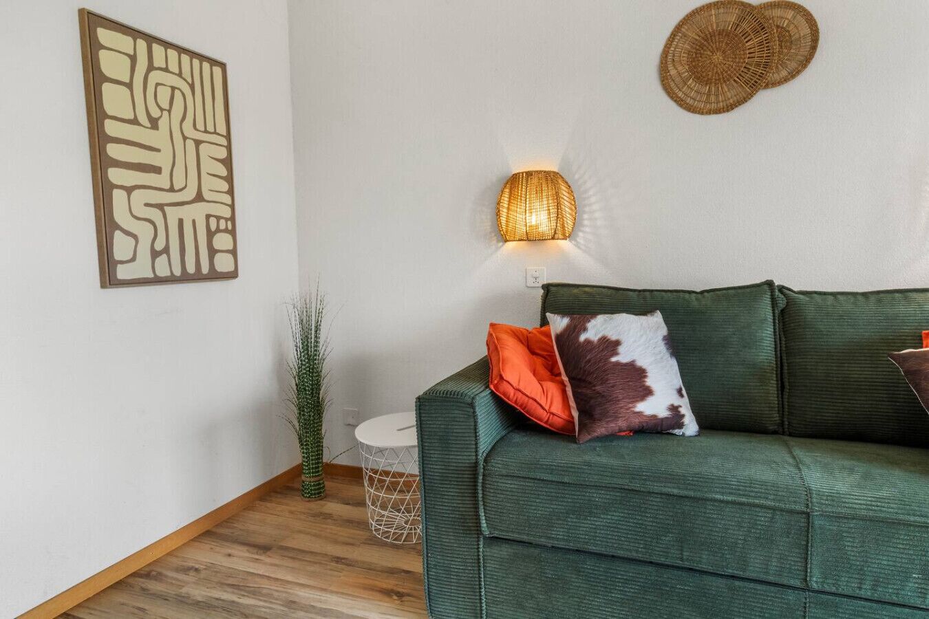 Un canapé vert agrémenté d’un coussin à motifs, un luminaire fixé au mur et un élément décoratif mural.
