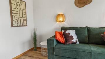 Un canapé vert agrémenté d’un coussin à motifs, un luminaire fixé au mur et un élément décoratif mural.