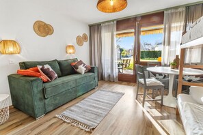 A cozy living room with a green sofa, a dining table, and a view of the outdoors. - Charmante chambre paisible près du lac de Neuchâtel (Portalban)