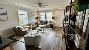 A spacious living room with a sofa set, coffee table, and a bookshelf filled with books. - Seven Peaks Escape - Breathtaking 180°+ Mountain Views | 2 Hot Tubs (Waynesville)