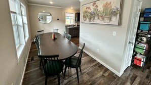 A dining area with a round table and chairs, a kitchen in the background, and a bookshelf with books. - Seven Peaks Escape - Breathtaking 180°+ Mountain Views | 2 Hot Tubs (Waynesville)