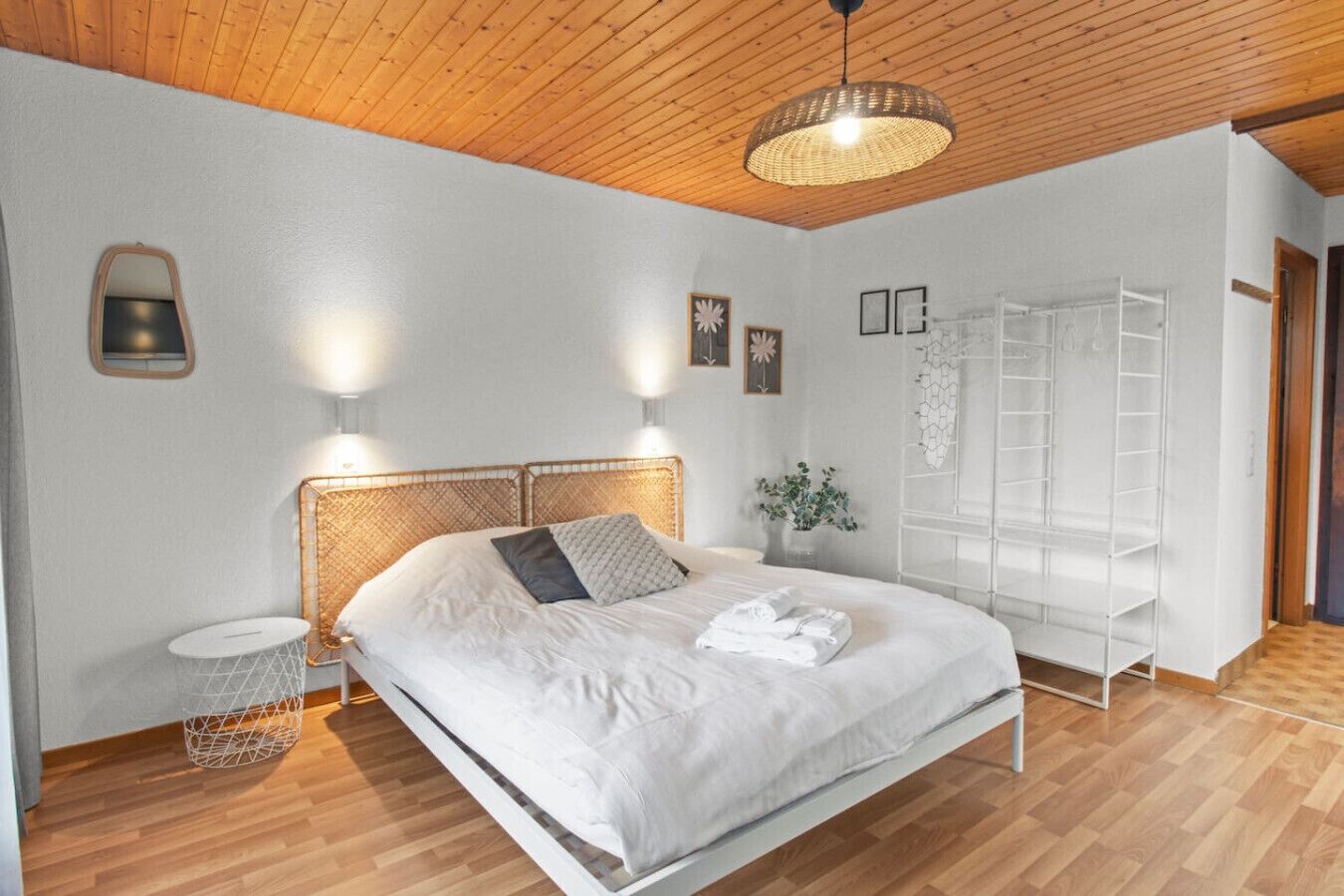 Une chambre à coucher bien rangée, avec un lit, des tables de chevet, un luminaire suspendu, une étagère fixée au mur et une armoire.