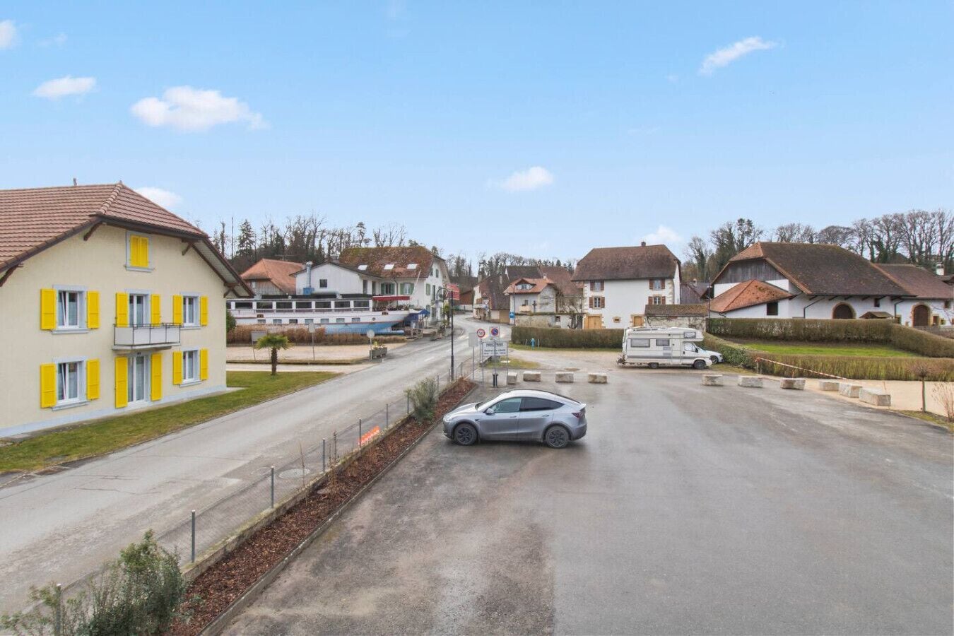 A residential street with houses, a parked car, and a boat docked at a pier.