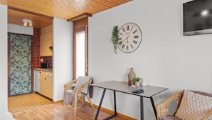 Ett modernt vardagsrum med ett träpanelat tak, ett matbord med stolar, en väggklocka och en tv som är monterad på väggen.
