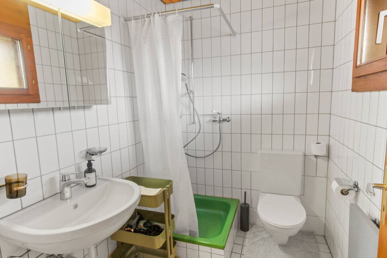 Ett litet badrum med handfat, toalett, dusch och ett grönt badkar.