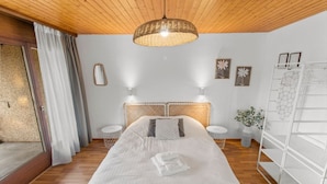 Ett sovrum med en säng, två sängbord, en hängande lampa, en spegel och en vit garderob.