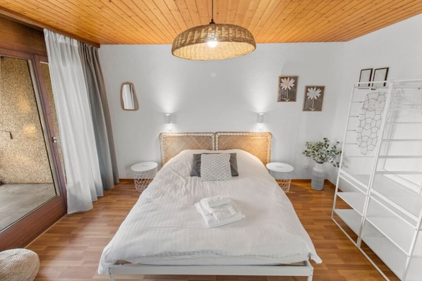 Ein Schlafzimmer mit einem Bett, zwei Nachttischen, einer Hängeleuchte, einem Spiegel und einem weißen Kleiderschrank.