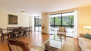 Amplia sala de estar con comedor, ventanas grandes y vistas al verde exterior.