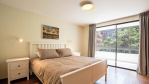 Un dormitorio con cama, mesitas de noche, un cuadro y un ventanal con cortinas.