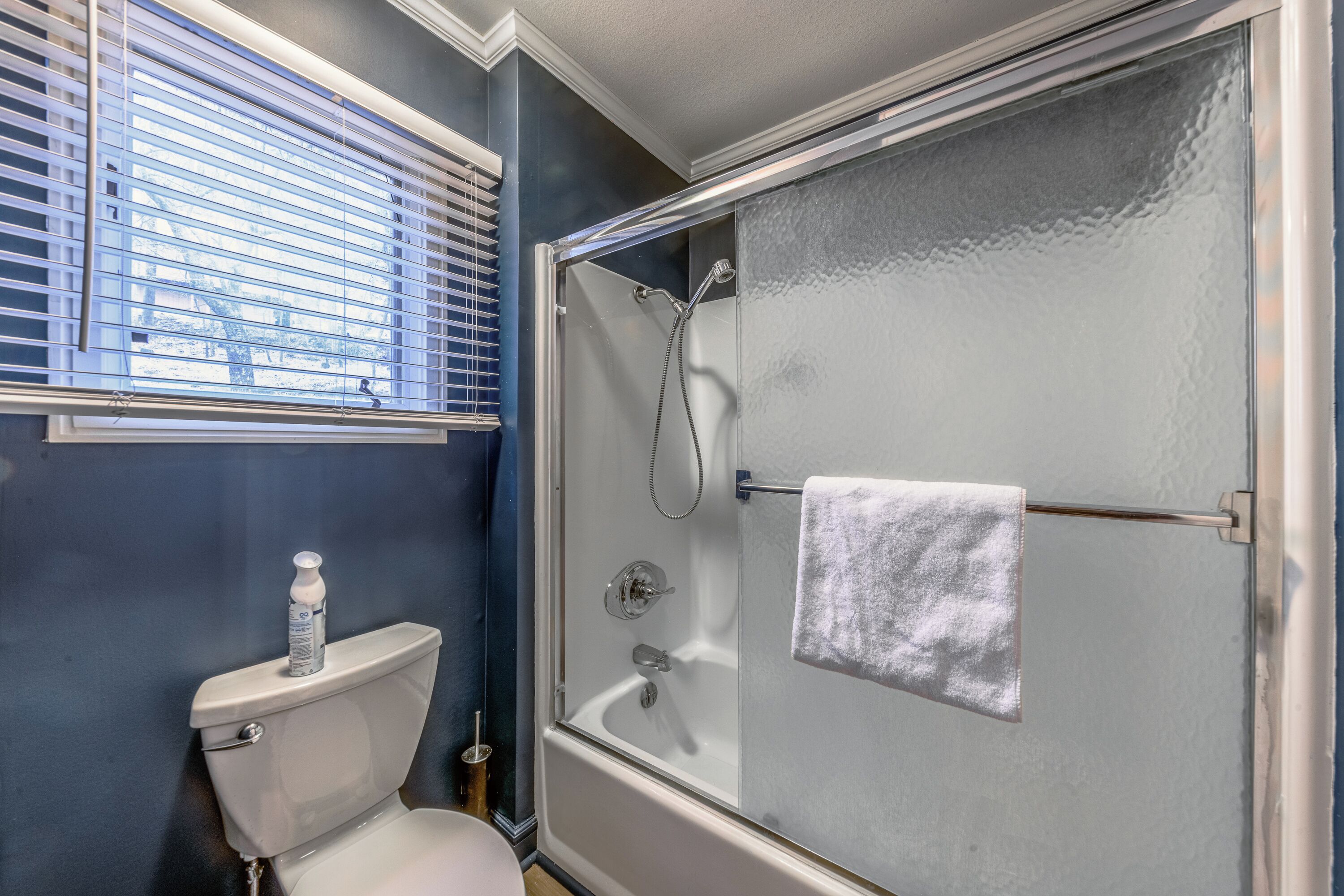 A bathroom with a glass-enclosed shower, a toilet, and a window with blinds.
