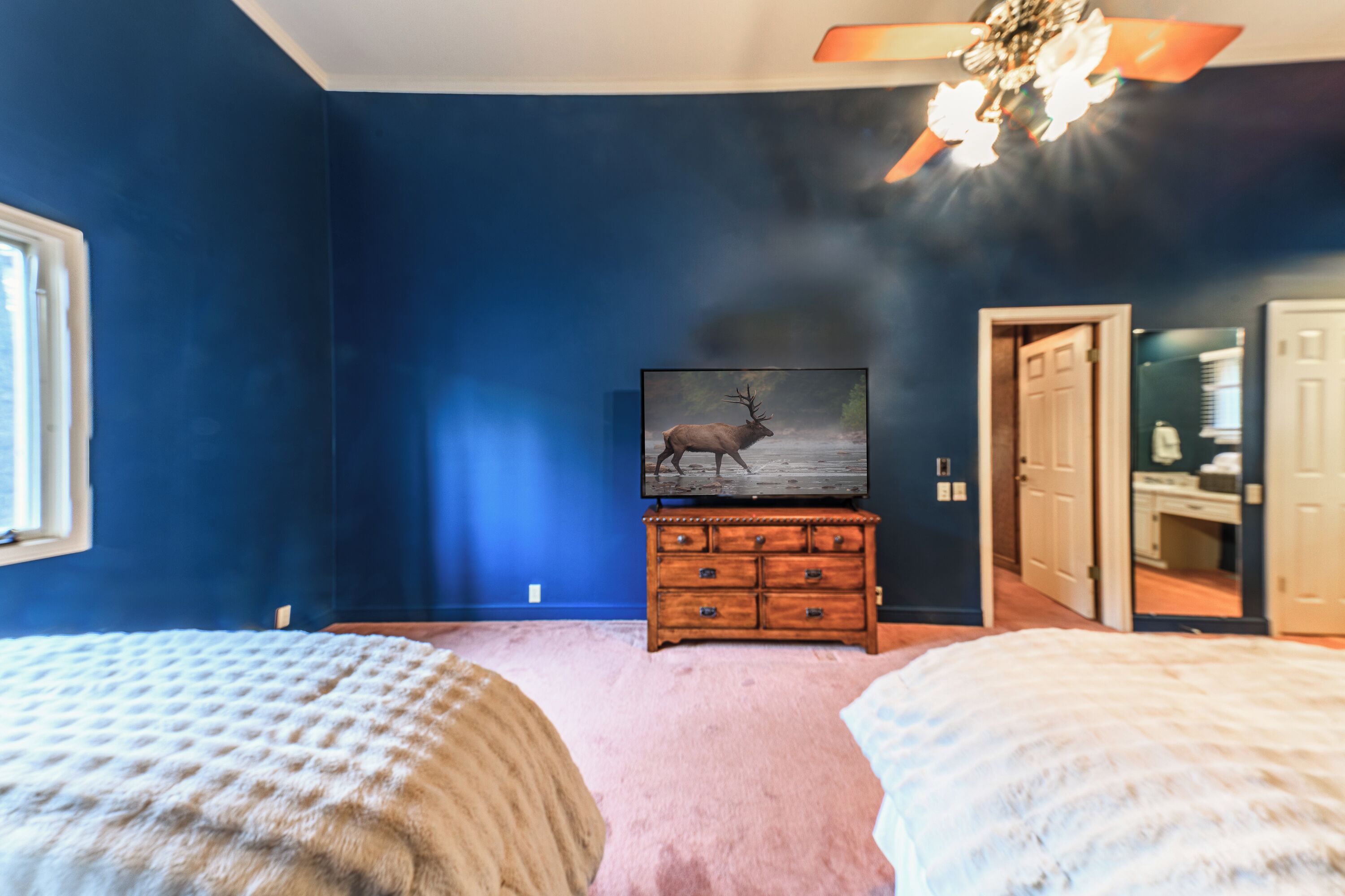 A bedroom with two beds, a dresser, a television, and a ceiling fan.