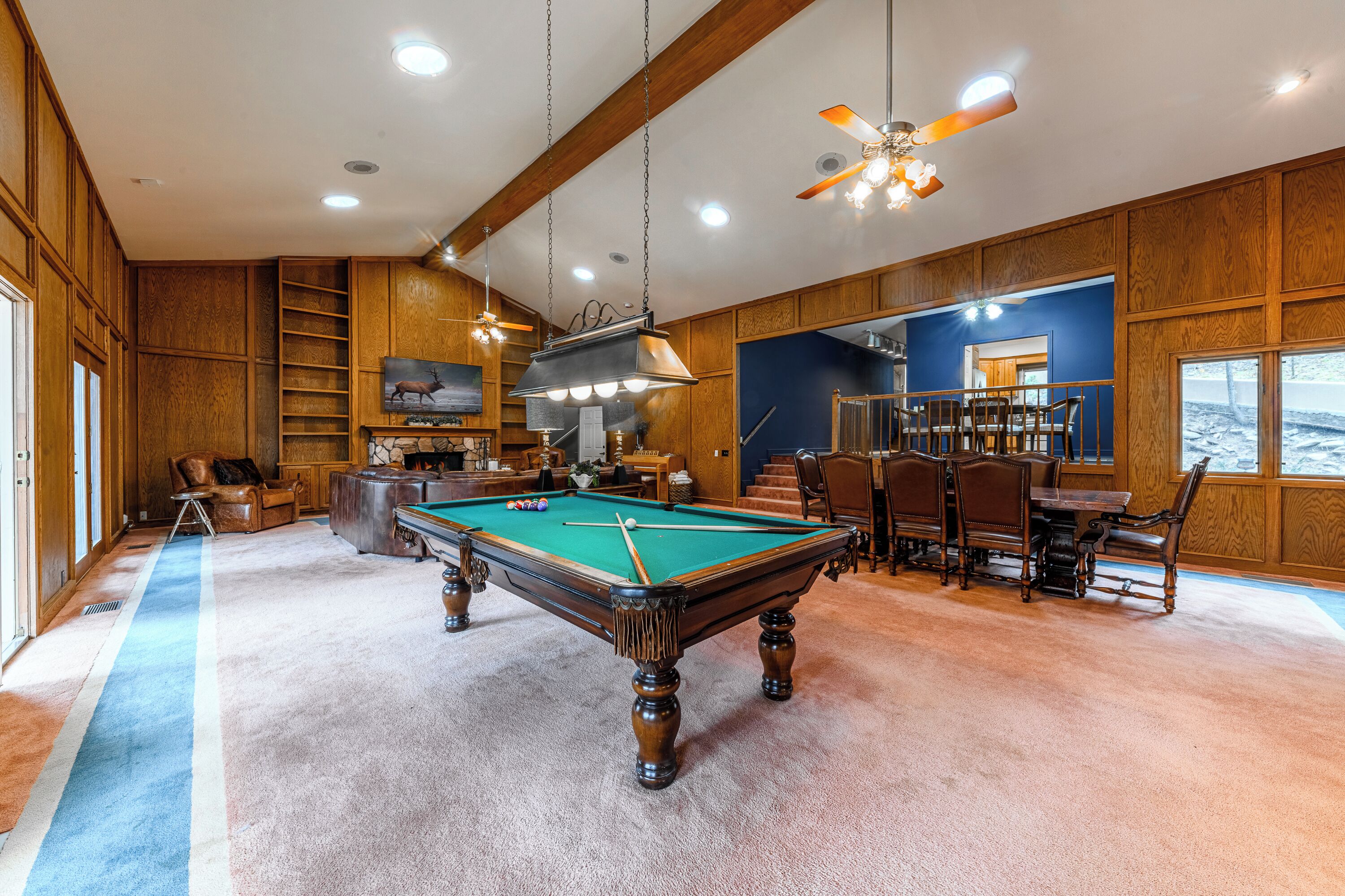 Une pièce spacieuse équipée d’une table de billard, de lambris en bois, d’un coin repas et d’une grande fenêtre offrant une vue dégagée.