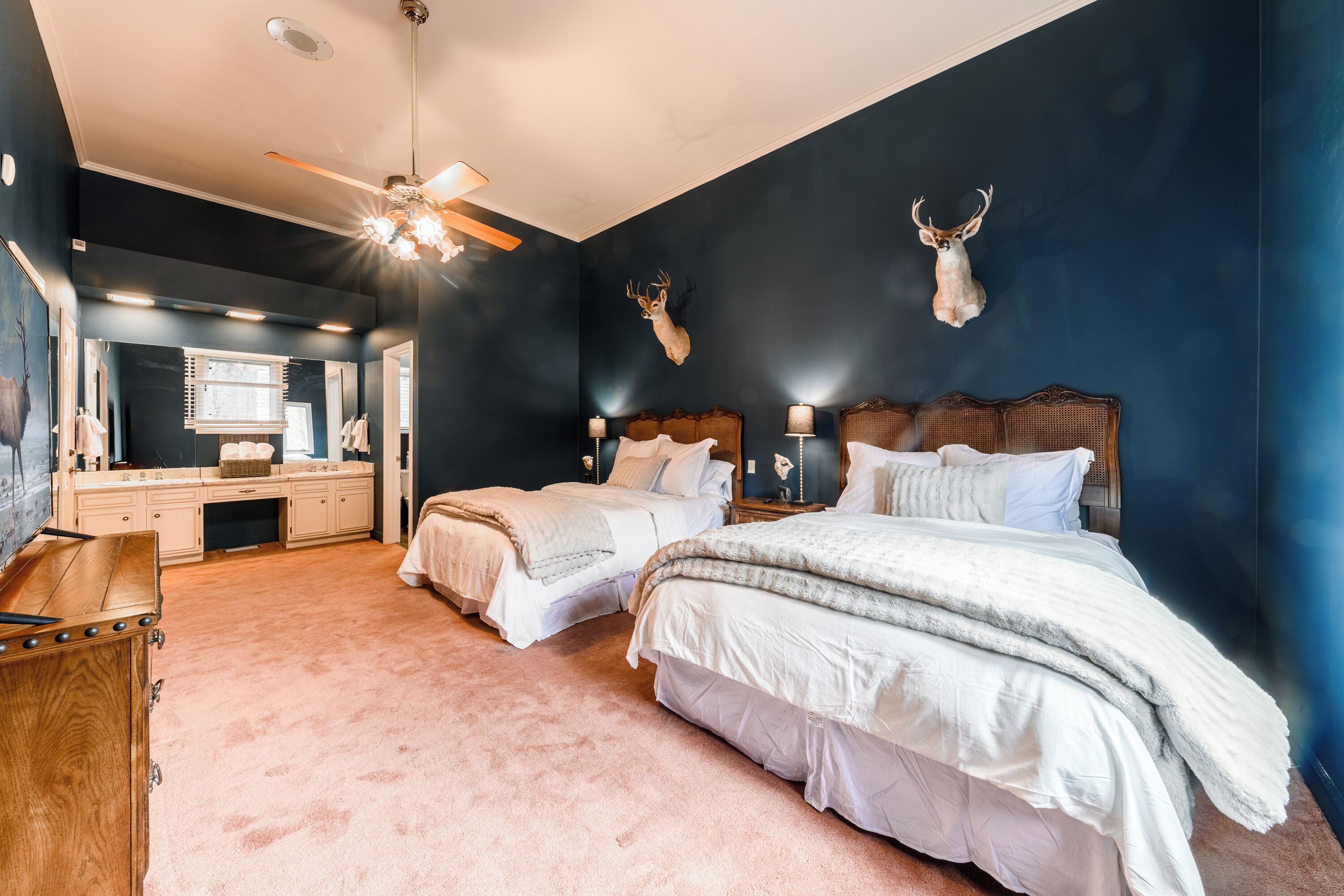 A bedroom with two beds, a vanity, and a ceiling fan.