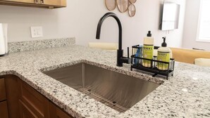 Una cocina con encimeras de granito, pileta de acero inoxidable, gabinetes de madera, grifo negro y dispensador de jabón en la encimera.