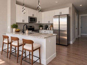 A modern kitchen with white cabinets, a stainless steel refrigerator, a built-in oven, and a marble countertop.
