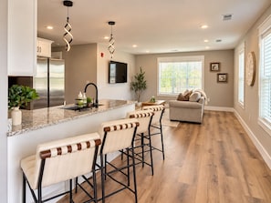 A modern kitchen with a central island, bar stools, a sofa, and a TV. - The Neyland Nest C (on UTK Campus, Free Parking) (Knoxville)