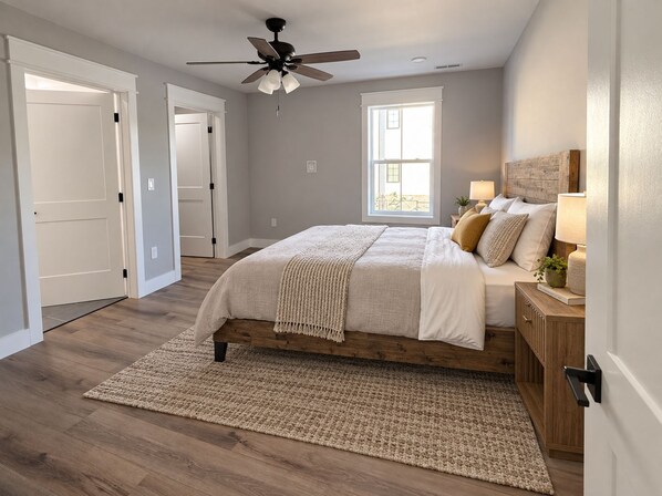 A bedroom with a bed, a ceiling fan, a window, and a nightstand with a lamp.